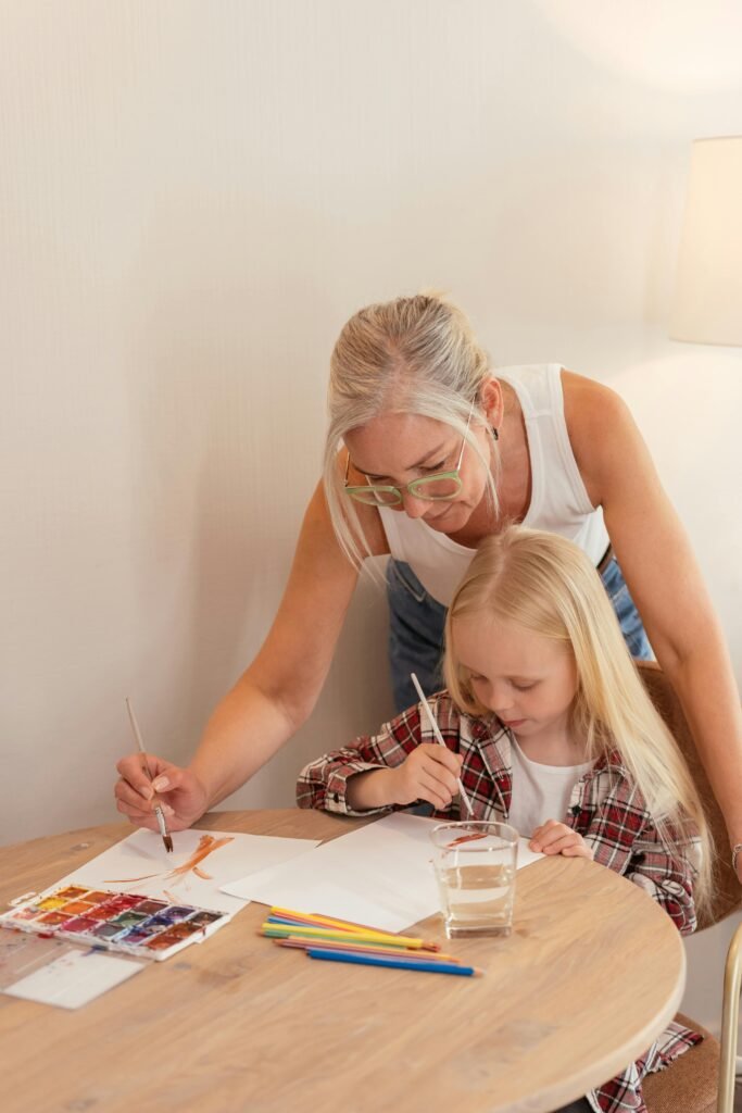 A grandmother and her granddaughter enjoying a painting session indoors.