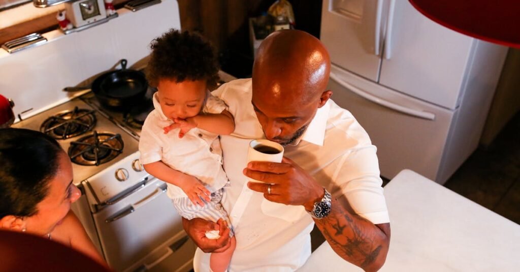 A father drinks coffee while holding his son in a cozy kitchen setting.